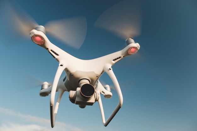 White drone hovering in a bright blue sky